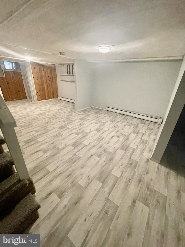 basement featuring light wood-type flooring, baseboard heating, and wood walls