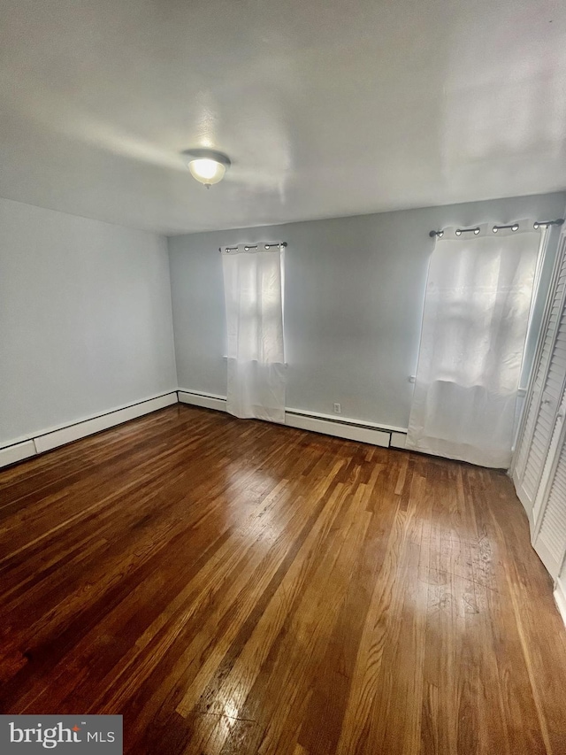 empty room with wood-type flooring and a baseboard heating unit