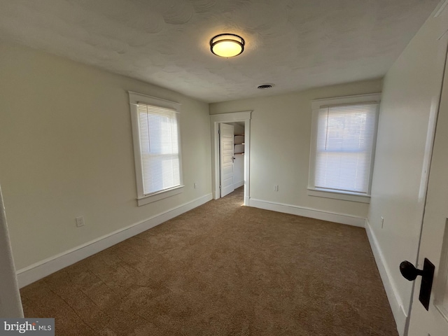 unfurnished bedroom featuring dark carpet, a textured ceiling, and a spacious closet