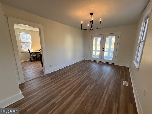 unfurnished dining area featuring a notable chandelier, dark hardwood / wood-style floors, a healthy amount of sunlight, and french doors