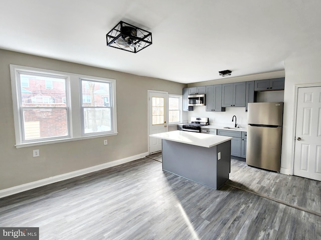 kitchen with sink, wood-type flooring, a center island, appliances with stainless steel finishes, and gray cabinets