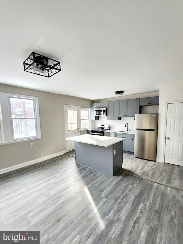 kitchen featuring sink, light hardwood / wood-style flooring, gray cabinetry, stainless steel appliances, and a center island