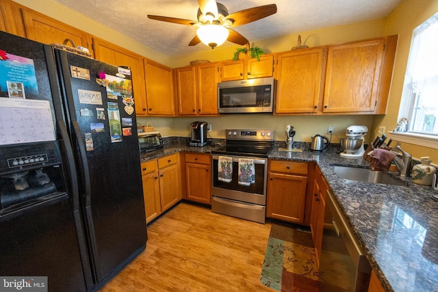 kitchen with sink, stainless steel appliances, light hardwood / wood-style floors, a textured ceiling, and dark stone counters