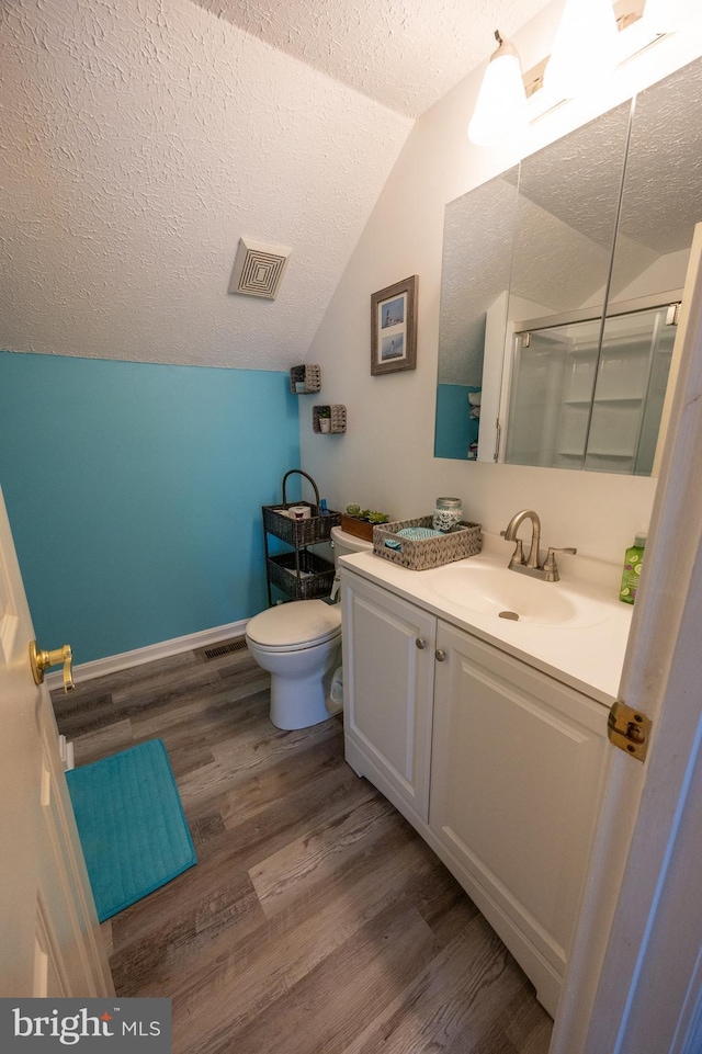 bathroom with vanity, wood-type flooring, a textured ceiling, vaulted ceiling, and toilet