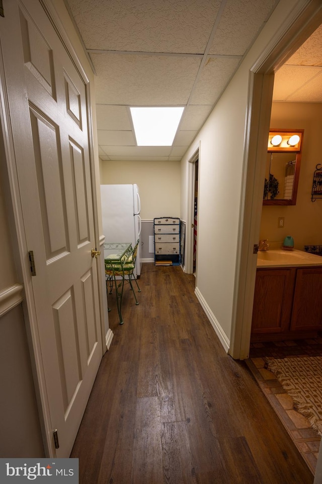 corridor with dark hardwood / wood-style flooring, sink, and a paneled ceiling