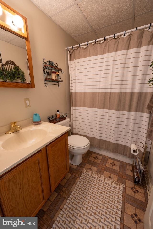 bathroom with a drop ceiling, vanity, a shower with curtain, and toilet