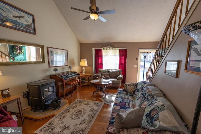 living room with ceiling fan, high vaulted ceiling, wood-type flooring, a textured ceiling, and a wood stove