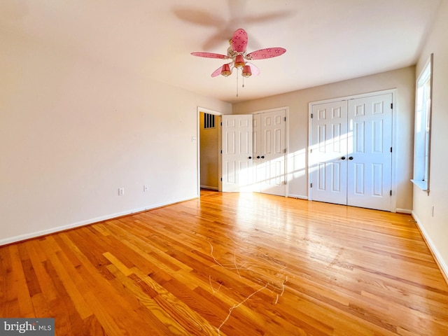 unfurnished bedroom featuring ceiling fan, light hardwood / wood-style floors, and two closets