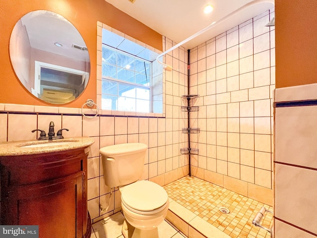 bathroom featuring tiled shower, toilet, tile walls, vanity, and tile patterned flooring