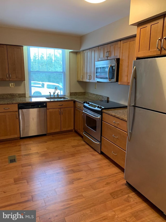 kitchen featuring stainless steel appliances, sink, dark stone countertops, and light hardwood / wood-style flooring