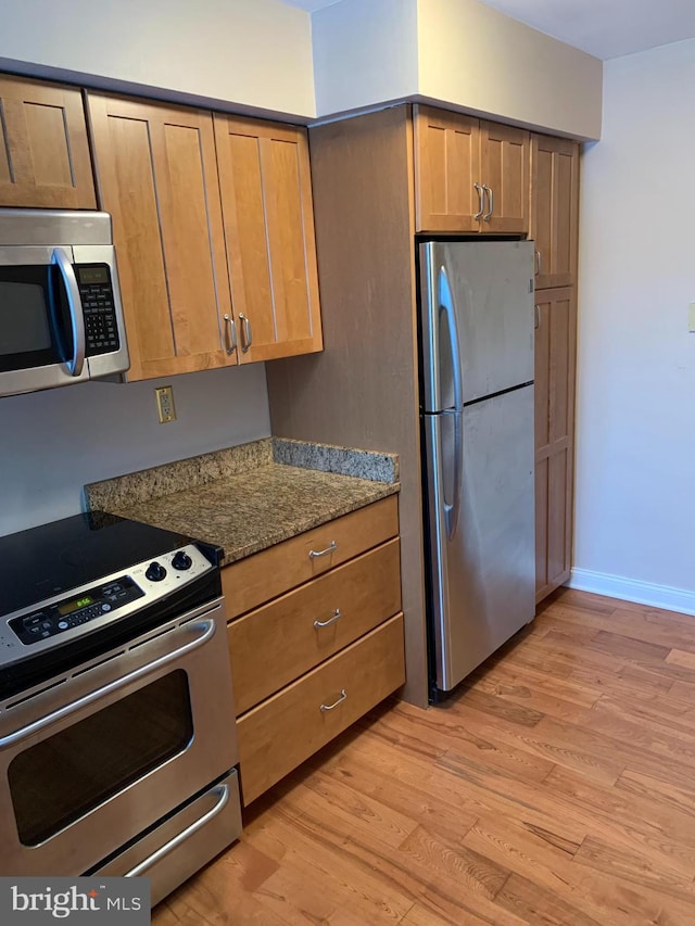 kitchen featuring light wood-type flooring, dark stone counters, and appliances with stainless steel finishes