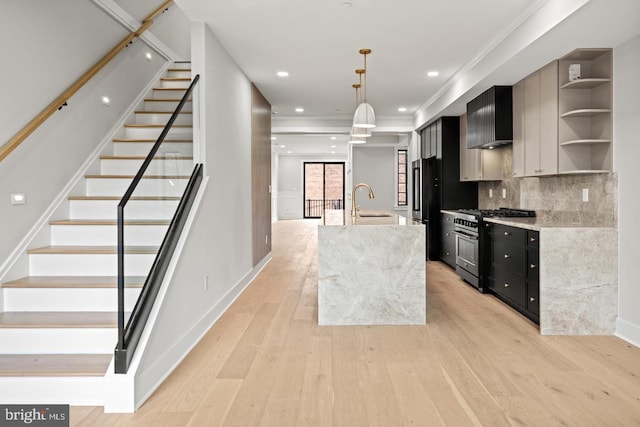 kitchen with high end stainless steel range, pendant lighting, tasteful backsplash, light hardwood / wood-style floors, and a center island with sink