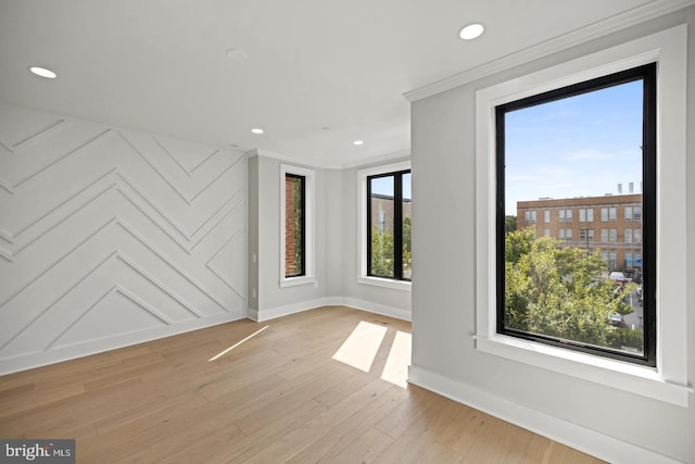 unfurnished room featuring light hardwood / wood-style floors, a wealth of natural light, and ornamental molding