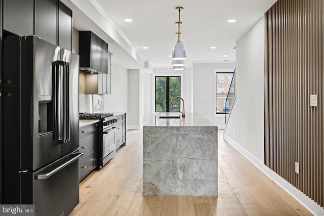 kitchen with light stone countertops, premium appliances, sink, decorative light fixtures, and a center island with sink