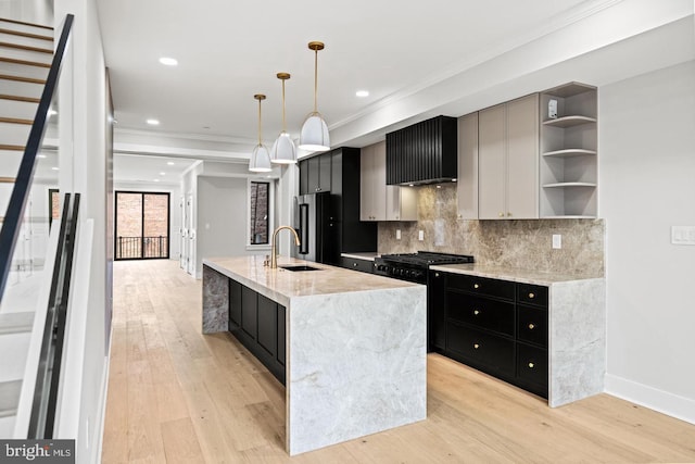 kitchen featuring light hardwood / wood-style floors, hanging light fixtures, black gas range oven, sink, and a center island with sink