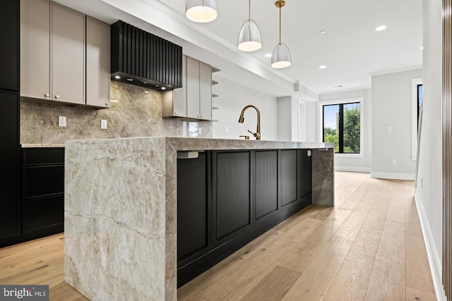 kitchen with light stone countertops, decorative backsplash, hanging light fixtures, light wood-type flooring, and a center island with sink