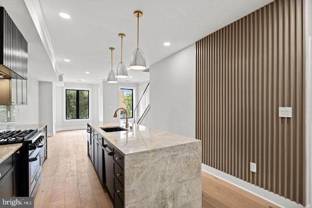 kitchen featuring decorative light fixtures, light stone countertops, a center island with sink, and gas stove