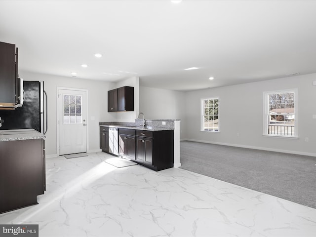 kitchen with appliances with stainless steel finishes, sink, light stone counters, dark brown cabinets, and light carpet