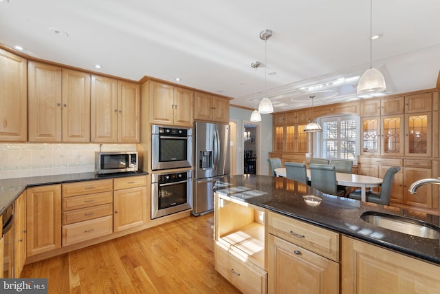 kitchen with pendant lighting, sink, appliances with stainless steel finishes, light hardwood / wood-style floors, and dark stone counters