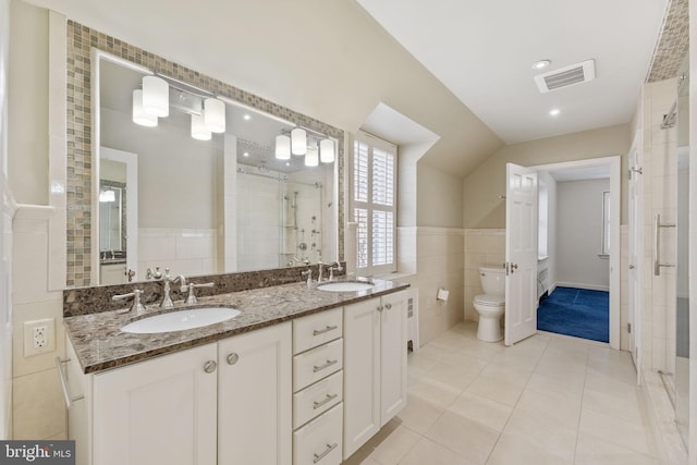 bathroom with a shower with door, tile walls, vanity, tile patterned floors, and toilet