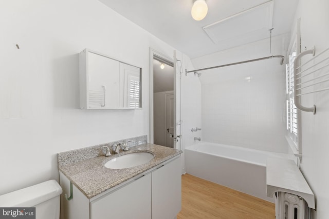 full bathroom with tiled shower / bath, radiator, hardwood / wood-style flooring, vanity, and toilet