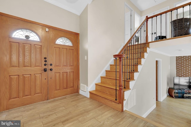 foyer entrance featuring a towering ceiling, ornamental molding, and light wood-type flooring