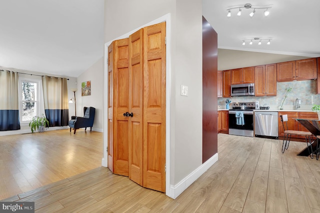 kitchen featuring appliances with stainless steel finishes, sink, light wood-type flooring, and decorative backsplash