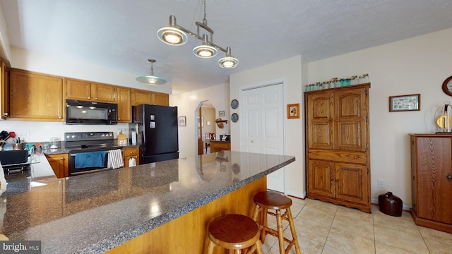 kitchen with a textured ceiling, black appliances, hanging light fixtures, light tile patterned floors, and a breakfast bar area