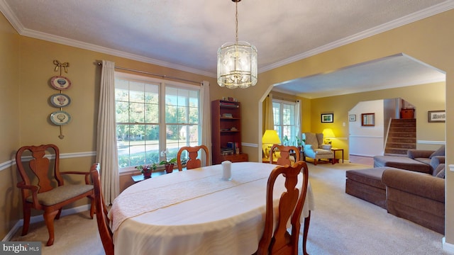 carpeted dining room with a textured ceiling, ornamental molding, and a chandelier