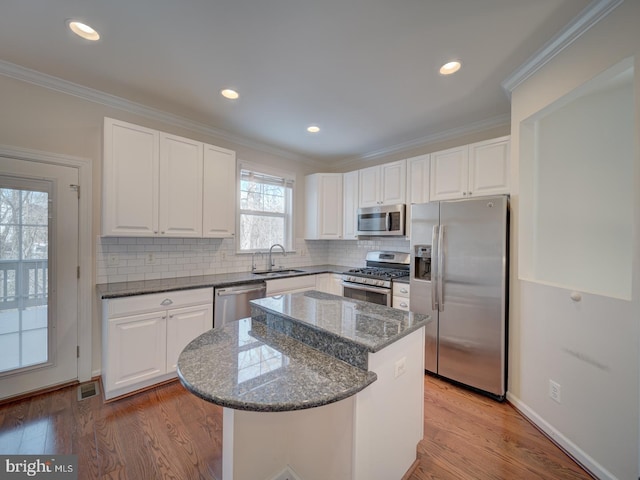 kitchen with sink, white cabinetry, appliances with stainless steel finishes, a kitchen island, and dark stone counters