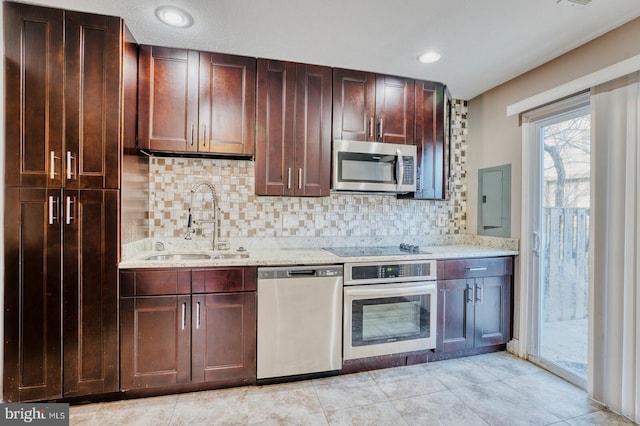 kitchen with light stone countertops, decorative backsplash, sink, stainless steel appliances, and electric panel