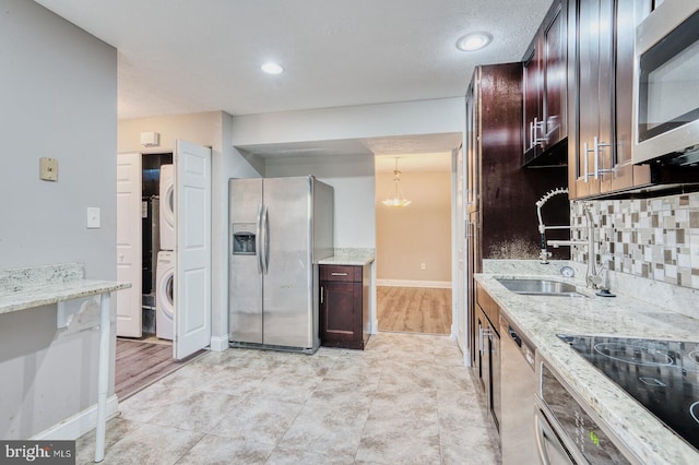 kitchen with hanging light fixtures, light stone countertops, stacked washing maching and dryer, and stainless steel appliances