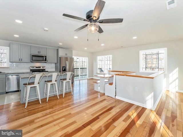 kitchen with stainless steel appliances, light stone countertops, gray cabinets, and decorative backsplash