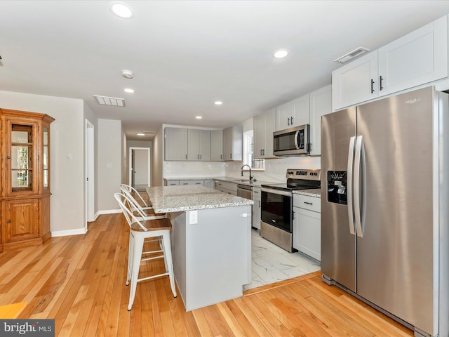 kitchen with sink, a breakfast bar area, appliances with stainless steel finishes, a kitchen island, and light stone countertops