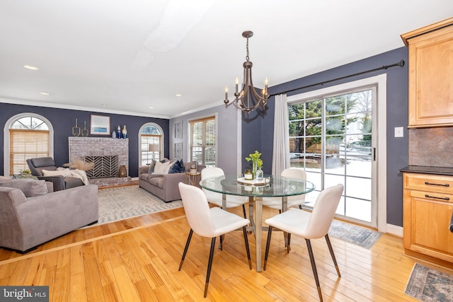 dining space with light hardwood / wood-style floors, ornamental molding, a notable chandelier, and a fireplace