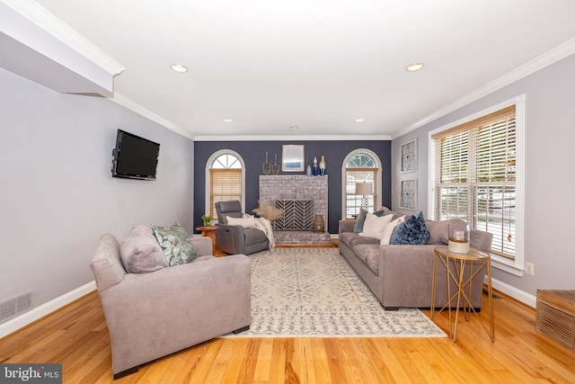 living room with wood-type flooring, ornamental molding, and a fireplace