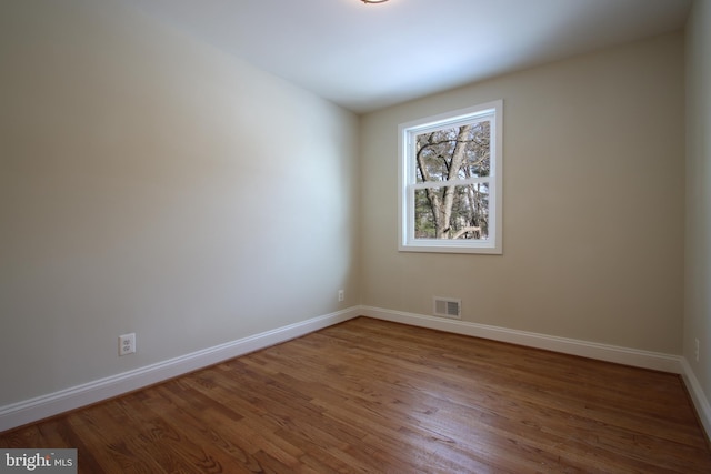 spare room with wood finished floors, visible vents, and baseboards