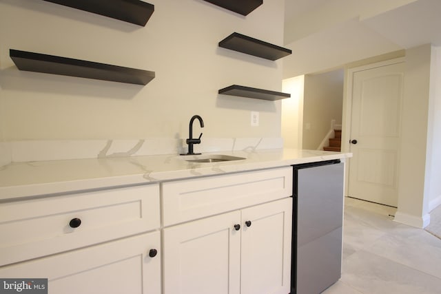 kitchen with open shelves, freestanding refrigerator, white cabinets, a sink, and light stone countertops