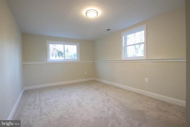 unfurnished room featuring a healthy amount of sunlight, visible vents, light carpet, and baseboards