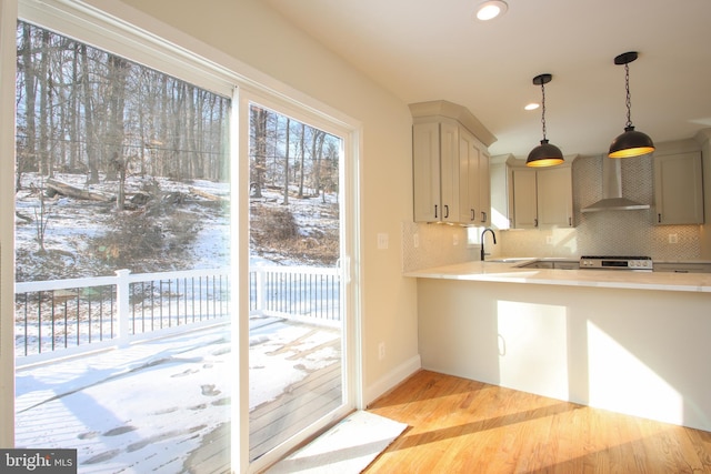 kitchen with sink, backsplash, hanging light fixtures, wall chimney exhaust hood, and light wood-type flooring