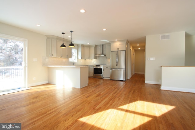 kitchen with visible vents, light countertops, appliances with stainless steel finishes, wall chimney range hood, and pendant lighting