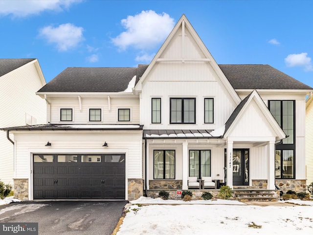 modern farmhouse featuring a porch, stone siding, driveway, and board and batten siding