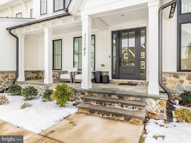 view of exterior entry featuring a porch, stone siding, and board and batten siding