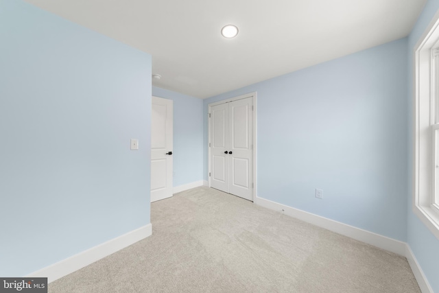 unfurnished bedroom featuring a closet, baseboards, and light colored carpet