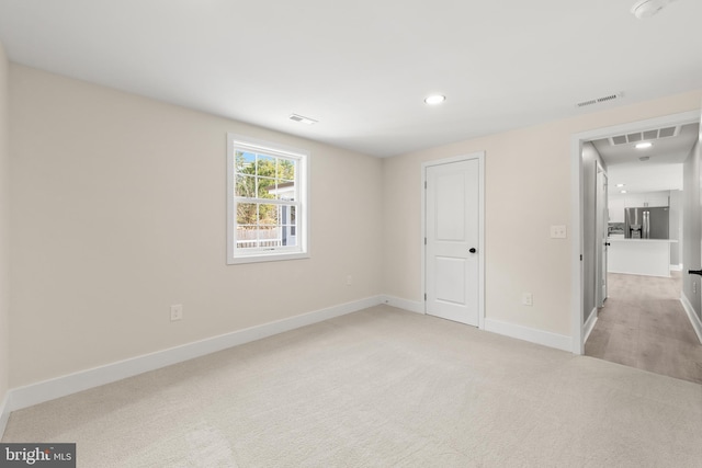 unfurnished bedroom with visible vents, light colored carpet, baseboards, and stainless steel refrigerator with ice dispenser