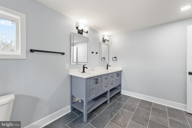 bathroom featuring double vanity, toilet, baseboards, and a sink