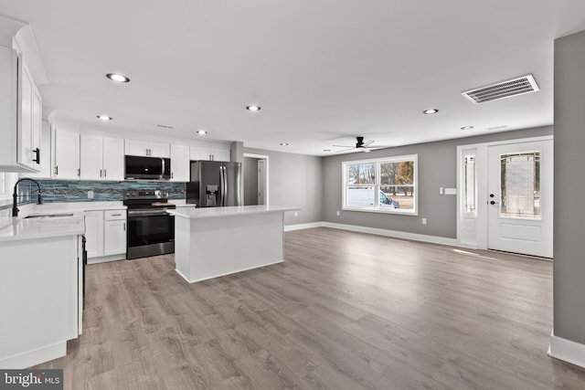 kitchen with tasteful backsplash, visible vents, a kitchen island, stainless steel appliances, and a sink