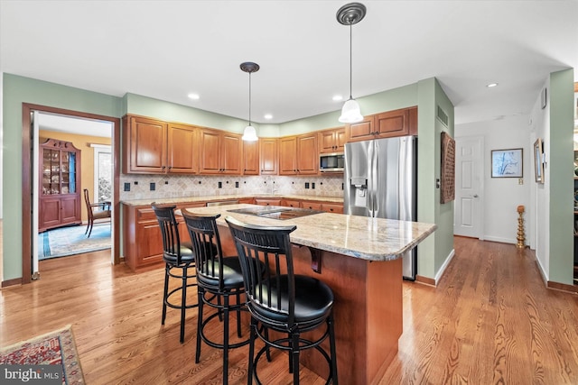 kitchen featuring a kitchen island, stainless steel appliances, hanging light fixtures, light wood-type flooring, and light stone counters