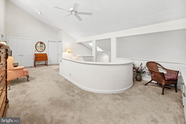 living area with light carpet, a textured ceiling, high vaulted ceiling, and ceiling fan