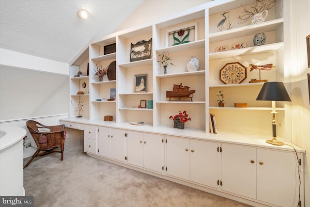 living area with vaulted ceiling, built in desk, light colored carpet, and a textured ceiling